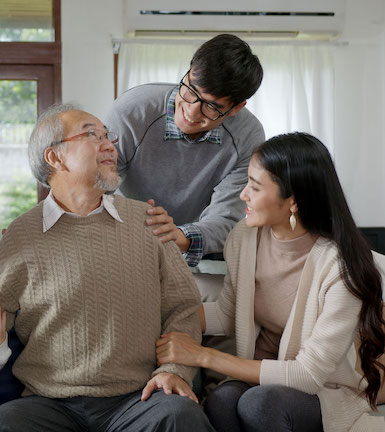 A healthy elderly Asian man sitting on a couch being caressed by his daughter and son