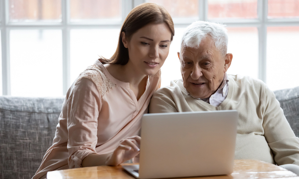 A young lady sitting with an elderly man while he views her laptop computer screen
